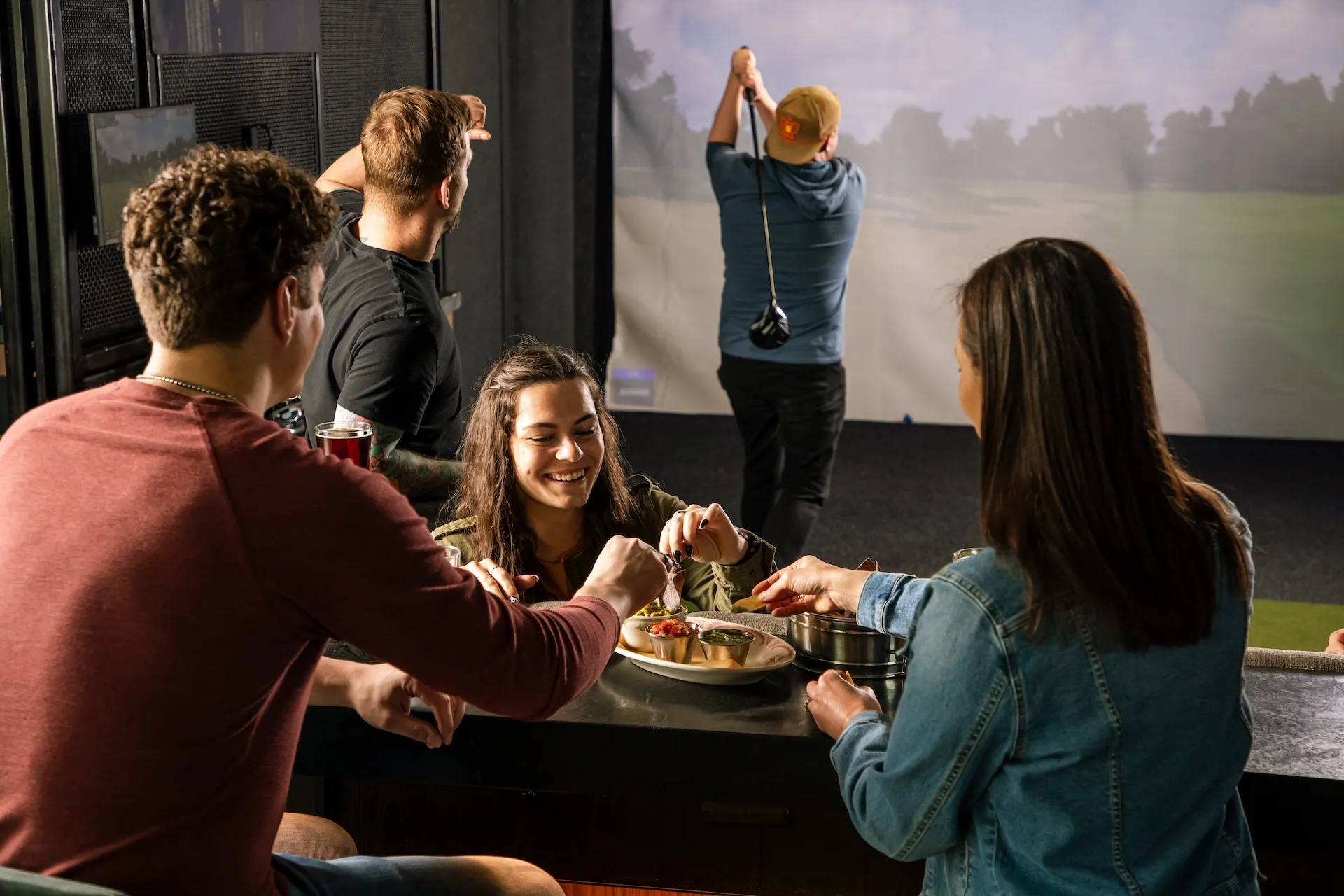 Group of men and women eating nachos and playing Topgolf